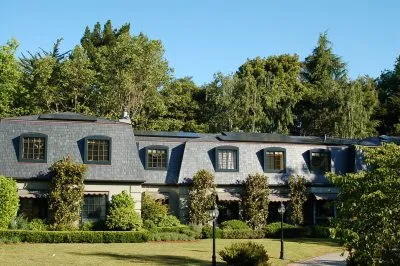 A large, elegant house with a dark shingled roof surrounded by trees, showcasing the roofing work by Mid-Peninsula Roofing Inc. in Burlingame.